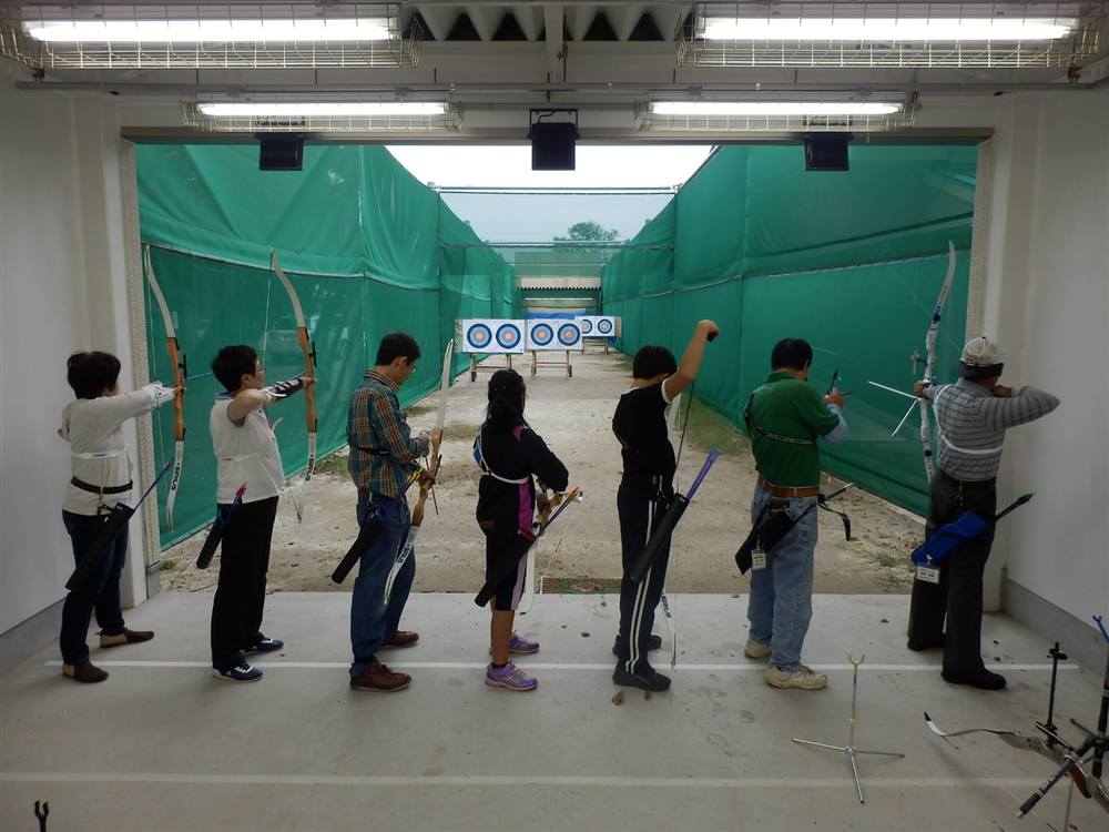 屋内のシューティングラインに並び、的に向かって弓を引く子どもから大人までの会員